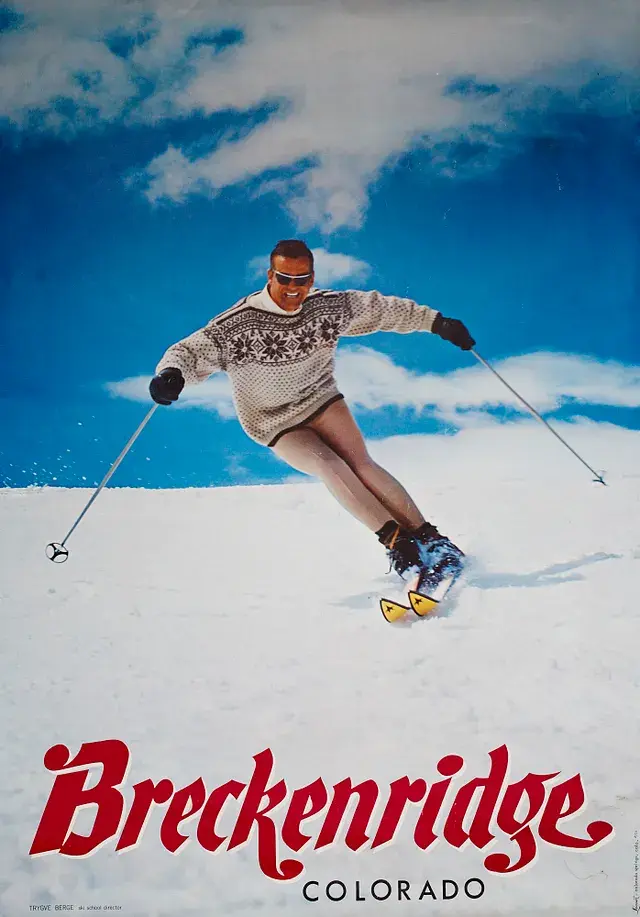 Skier in a sweater and shorts carving through snow under a blue sky. "Breckenridge Colorado" text in bold red at the bottom.