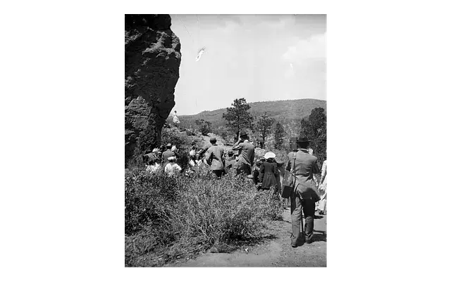 Group of people hiking along a rocky path surrounded by wilderness and distant hills under a clear sky. The mood is adventurous.