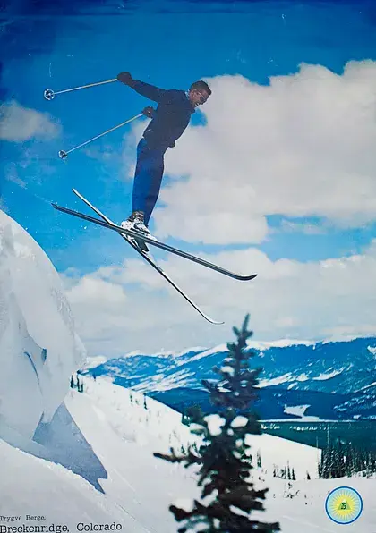 Skier mid-air doing a jump against a clear blue sky and snowy landscape at Breckenridge, Colorado. Text: Breckenridge, Colorado.