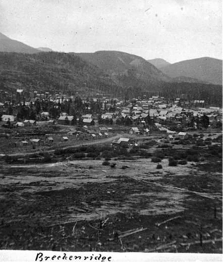 Historic black-and-white photo of Breckenridge, showing a small town with scattered houses, surrounded by hills and trees under a cloudy sky.