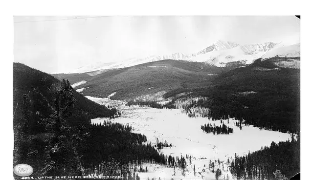 Snow-covered valley surrounded by forested mountains, with a clear sky above. Text at bottom reads: "7665, Up the Blue, Near Breckinridge."