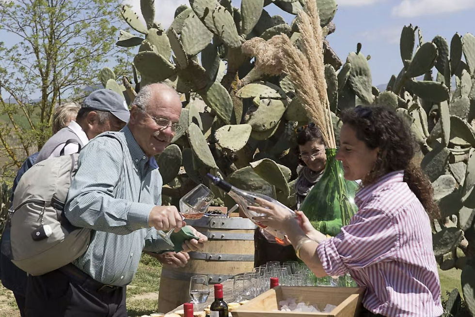 outdoor with cactus in background, man with backpack tilting wine glass for woman in red striped blouse to pour from wine bottle