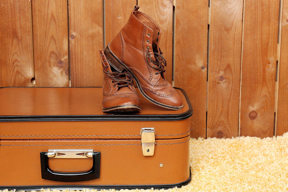 brown boots sitting on top of old brown suitcase in front of wood paneling and beige carpet