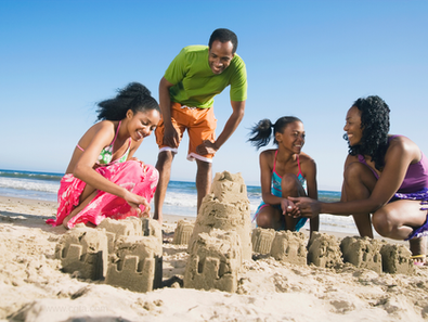 African American man, woman, two girls building a sand castle on a beach, ocean and sky in background
