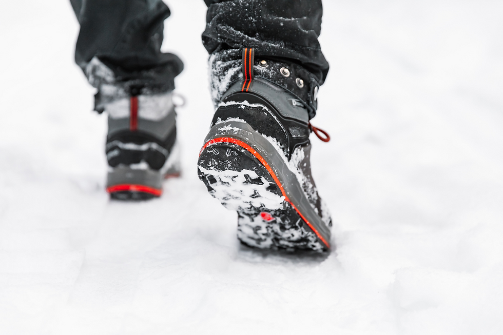 feet in gray and black snow boots and black jeans on legs walking through snow