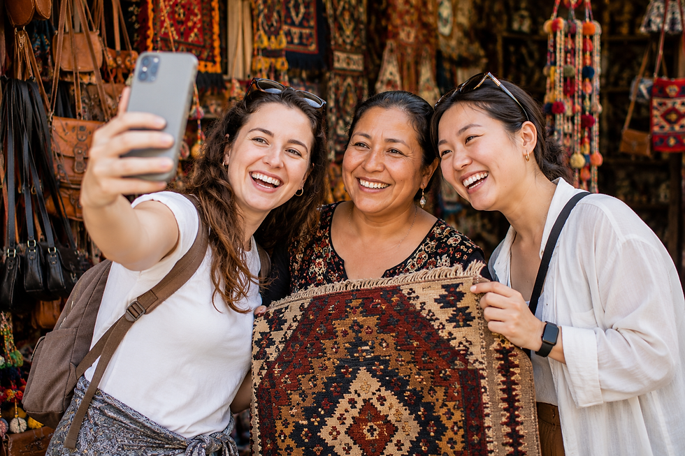 White and Asian female travelers taking a selfie with a female market merchant while holding a handcrafted rug they purchased in a colorful marketplace.