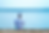 man wearing blue shorts, white t-shirt, white bucke hat sitting on beach looking over ocean
