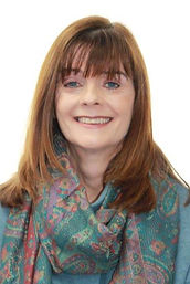 Portrait of Maggie, a professional reflexologist, smiling and wearing a colorful scarf and blue top, set against a white background.