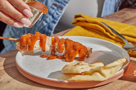 Close-up of Tasty Bite® butter chicken sauce being poured over a chicken kabob.