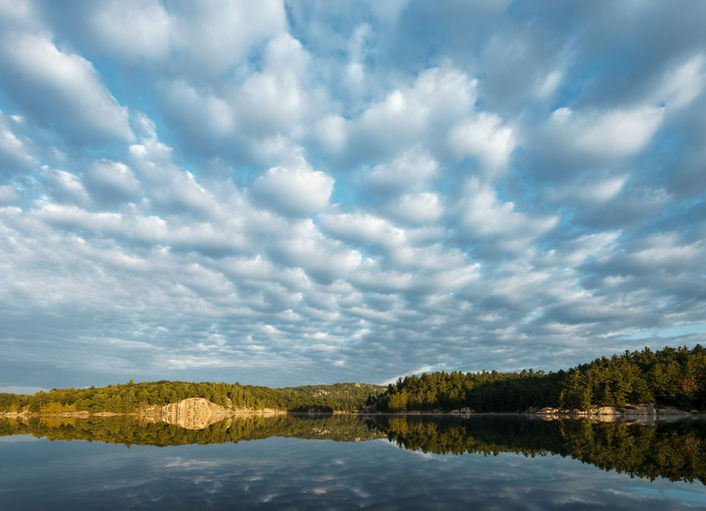 Lake under cloudy sky reflecting the forest and the horizon. devinshots.