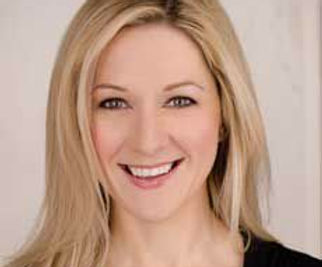 Image of woman with long blonde hair faciing the camera and smiling. She wears a black round neck top and has green eyes.