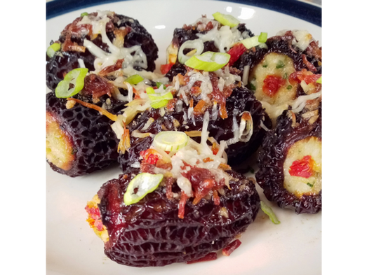 Wild harvested, crab stuffed morel mushrooms topped with a parmesan breadcrumb crust and green onion on white ceramic plate.
