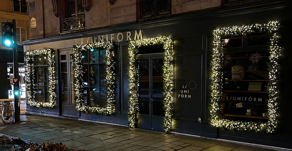 Façade de la boutique L/UNIFORM à Paris 7e décorée pour Noël avec sapin naturel, trois vitrines encadrées, une porte illuminée et câblage totalement invisible