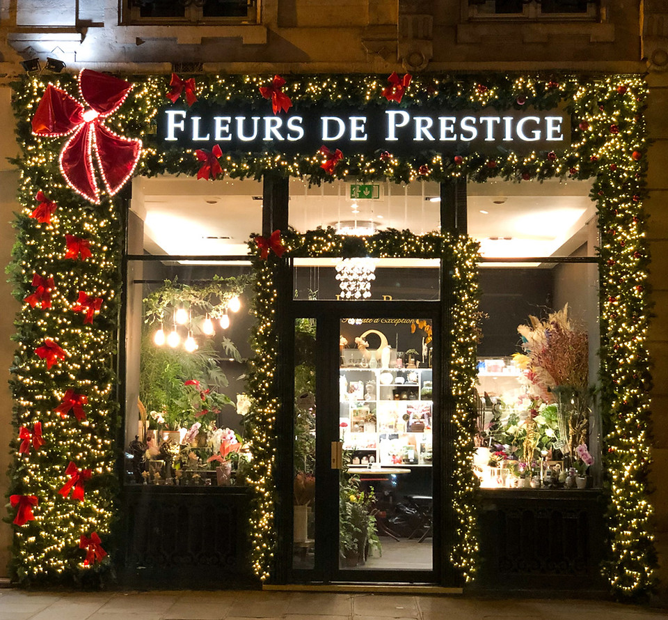 Décoration de Noël de la boutique Fleurs de Prestige à Paris 9e avec encadrement lumineux en sapin naturel et nœuds rouges