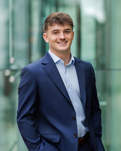 Relaxed outdoor corporate headshot of a male professional wearing glasses, photographed in natural light with a friendly, approachable expression.