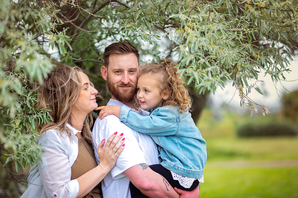 Parents hugging their child beneath trees during a natural family photography session in Suffolk
