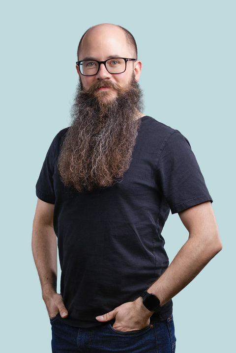 Relaxed personal branding headshot of a male professional with a beard, photographed against a light blue studio background.