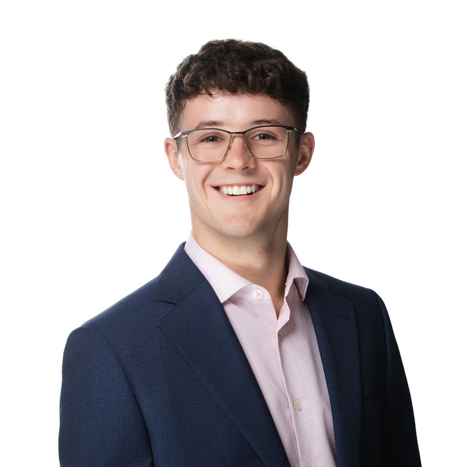 Professional headshot of a young male business professional in a navy blazer, clean white background with a modern corporate look.