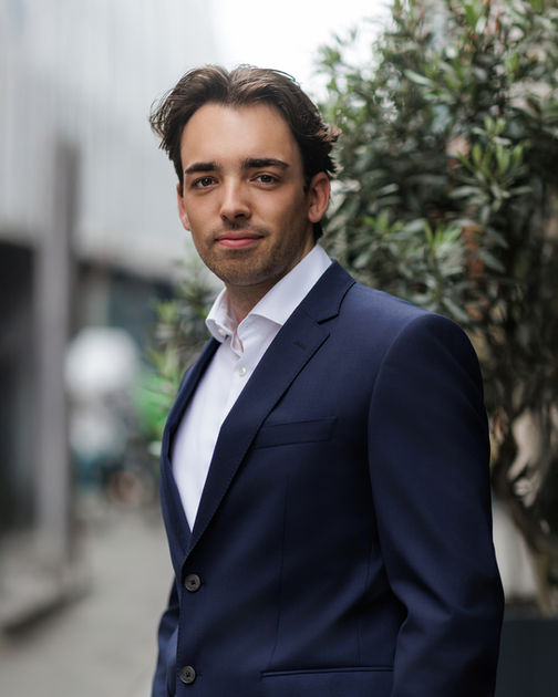Natural outdoor corporate headshot of a male professional in a navy suit, modern business portrait photographed in an urban Bristol setting.