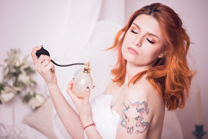 Soft boudoir portrait of a red-haired woman holding perfume, feminine and romantic style