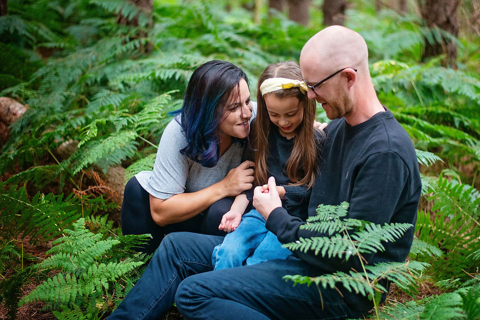 Family cuddling among ferns during an outdoor woodland photoshoot in Suffolk