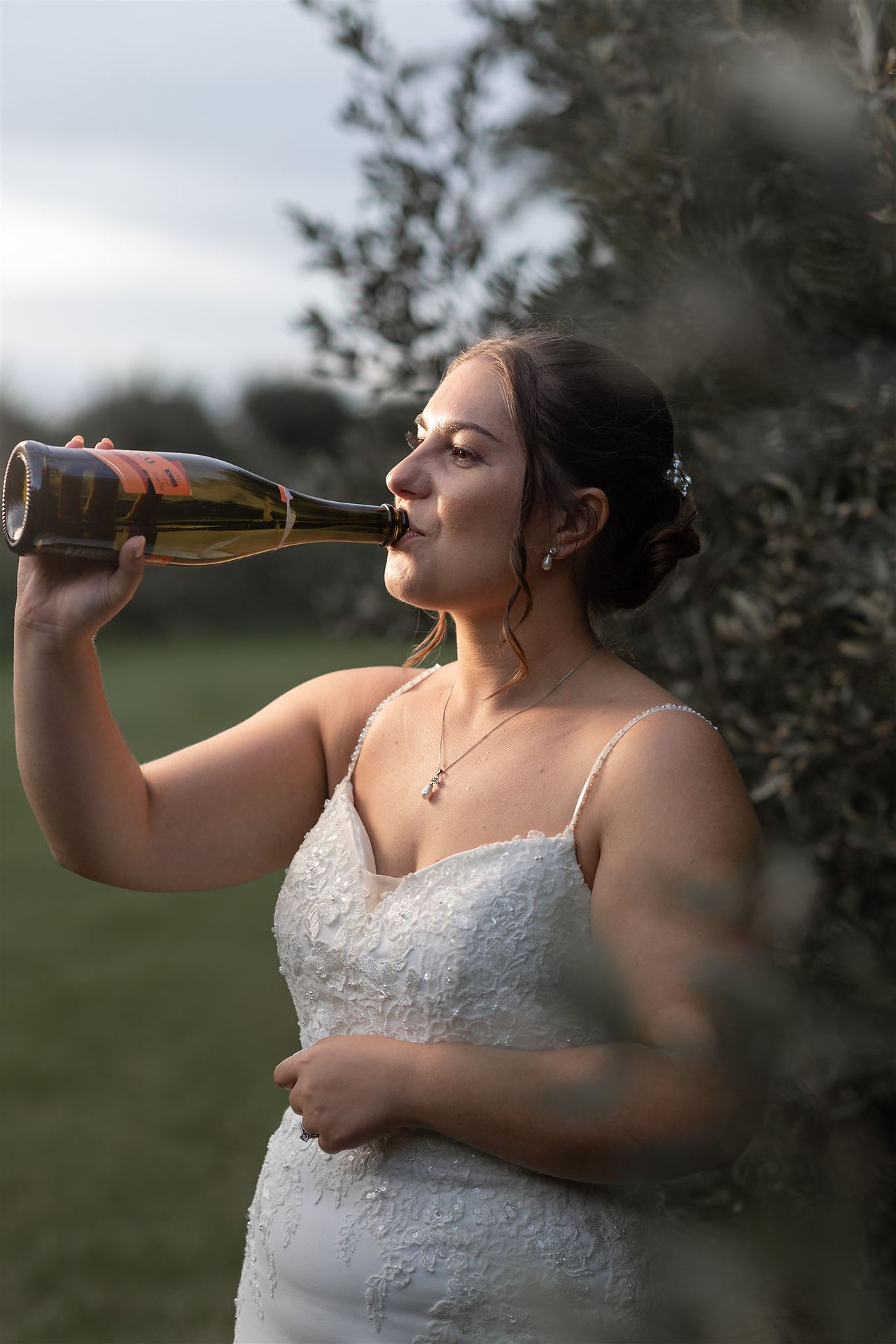 Fun alternative wedding photography of the bride drinking from a bottle outdoors