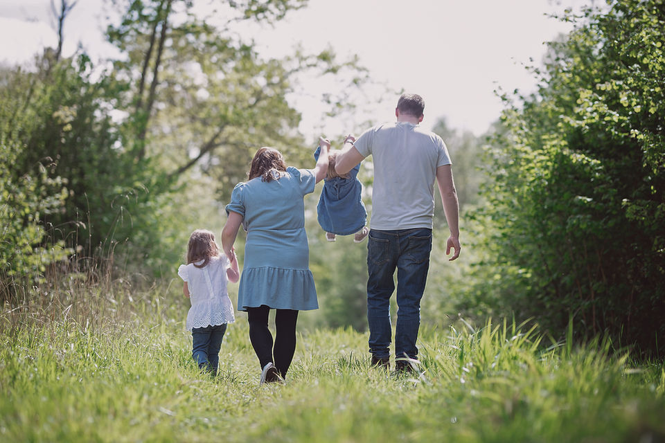 Family walking hand in hand through woodland during an outdoor family photoshoot in Suffolk