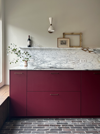 Interieuradvies Rotterdam met Bordeaux rode keuken met marmeren aanrechtblad en waaltjes op de vloer met wandlampjes en walnoten maatwerkbankje