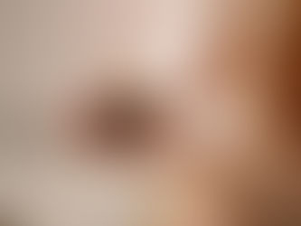 A person with dark nails holds a lit candle in a small ceramic holder. The setting is soft and serene, with a neutral background.