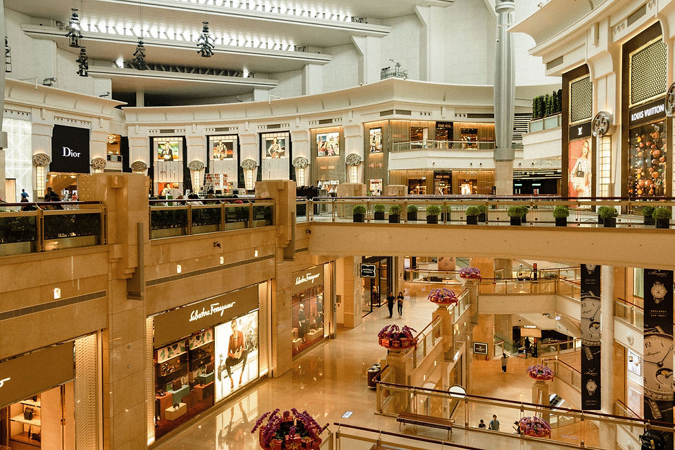 Bright luxury mall interior with Dior, Louis Vuitton and Salvatore Ferragamo storefronts; a few shoppers walk among beige balconies.