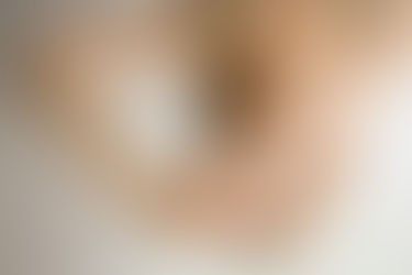 Blurry image of a person holding a small mirror reflecting a focused blue eye, surrounded by soft neutral tones.