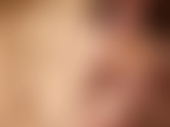 Woman in sunglasses lounging on a wooden chair, sipping a fruity drink. She wears a brown swimsuit. Sandy beach background. Relaxed mood.