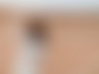 Woman in a white outfit holds a "Stop" sign, raising her fist, against a beige backdrop. She appears determined and passionate.