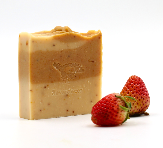 Jabón facial de fresa natural junto a fresas sobre fondo blanco