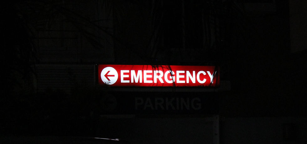 Red "Emergency" sign with white arrow pointing left, glowing in a dark setting. Faint "Parking" text is visible below. Quiet, urgent mood.
