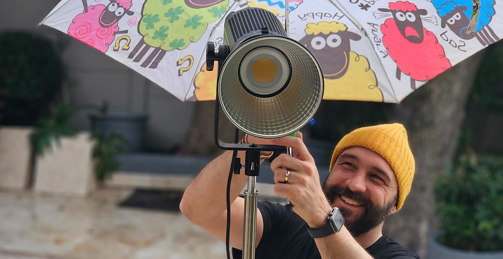 Smiling man in yellow beanie adjusts a studio light under a colorful sheep-patterned umbrella with Happy text.