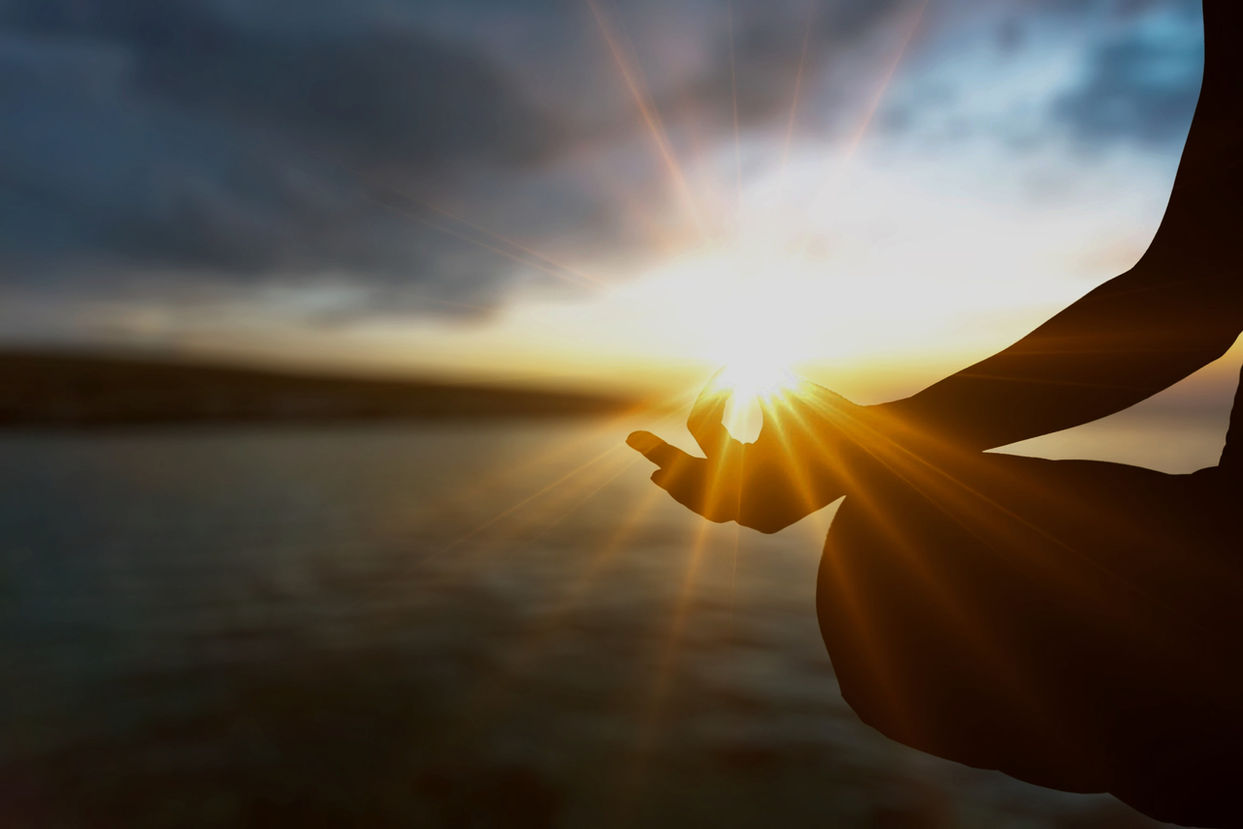 A woman sits near water in meditation and practising breathwork to relieve anxiety and stress.