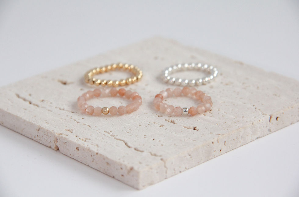 Four rings on a stone surface; gold, silver, and two gemstone bands. Kleynot Jewellery