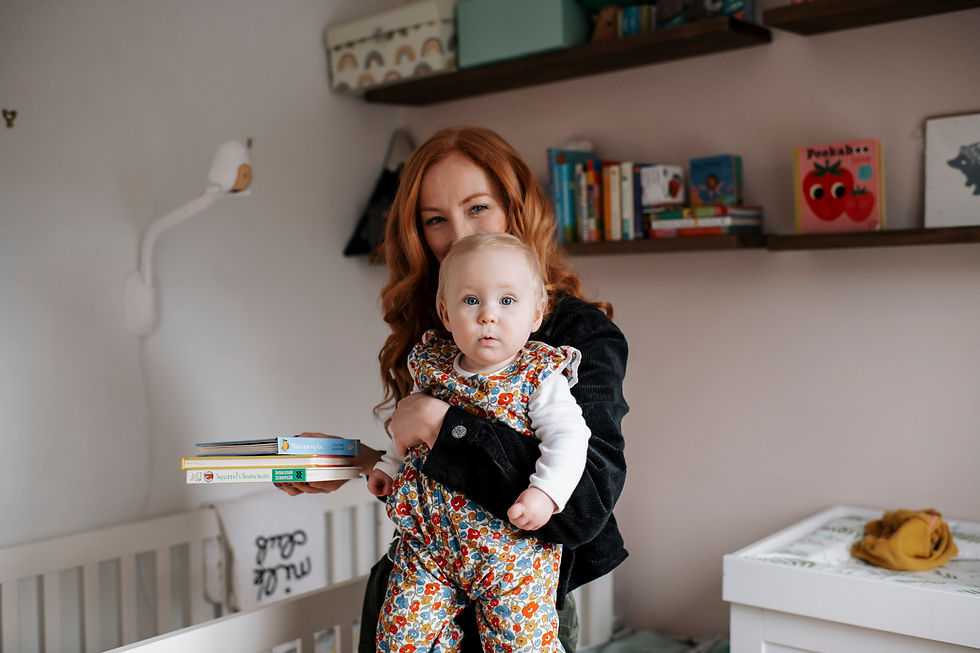 Woman holding baby in floral outfit, standing in a cozy nursery with books and children's decor. Natural family shoot at home Newcastle | Angela Fenwick Photography