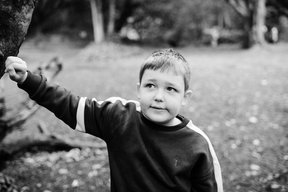 Boy in a dark sweatshirt, holding a tree branch in a wooded area. Black and white image creates a calm and thoughtful mood. Outdoor family shoot Newcastle | Angela Fenwick Photography