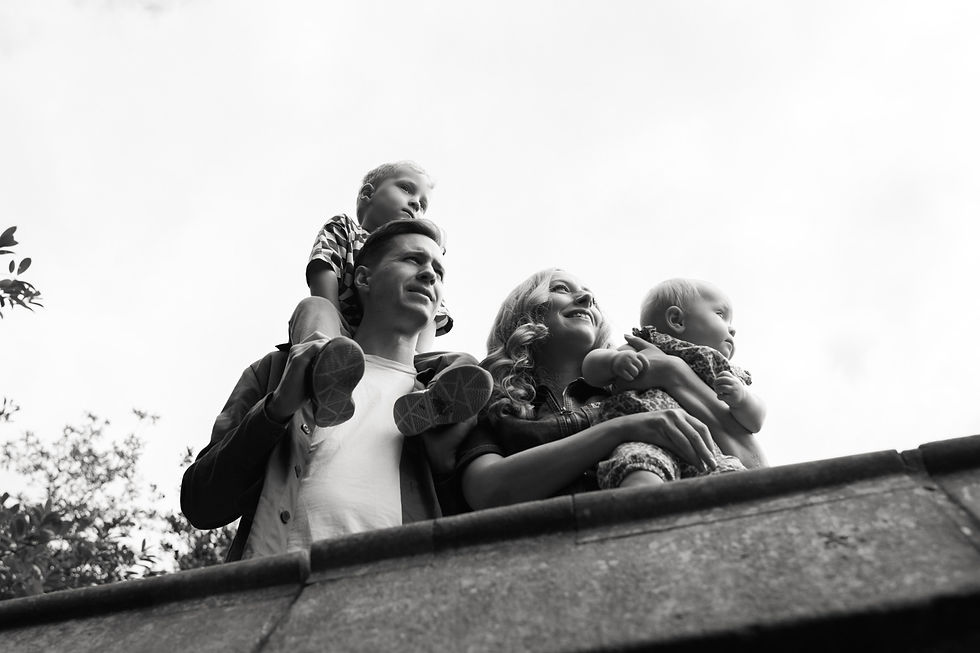 Family looking happily upward, father with child on shoulders, mother holding baby. Black and white, outdoors with trees in background | family photos newcastle | Angela Fenwick Photography