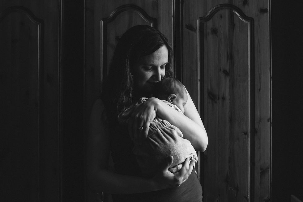 A woman gently cradles a baby in a dimly lit room with wooden doors | newborn photos Newcastle | Angela Fenwick Photography