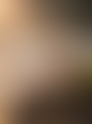 Eine Frau, Mitte 50 mit kurzen, glatten, leicht grauen Haaren, sitzt auf einem Stein, an einem Bach. Sie trägt ein langes, dünnes, hellbraunes Sommerkleid. Ihre Augen sind geschlossen, sie denkt nach. Es sind Steine im Bachbett zu sehen. Hinter ihr befinden sich früne Pflanzen. Im Bach spiegelt sich das Sonnenlicht. Oben links, scheint schemenhaft Sonnenlicht in das Bild. gedanken-loslassen-lernen.