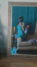 a mirror selfie of a dominatrix in a jean dress sitting on the side of a couch