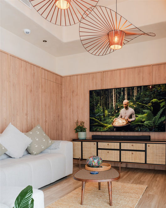 Warm living room interior with full-height oak wall panelling, oversized copper pendant lights, and rattan media unit.