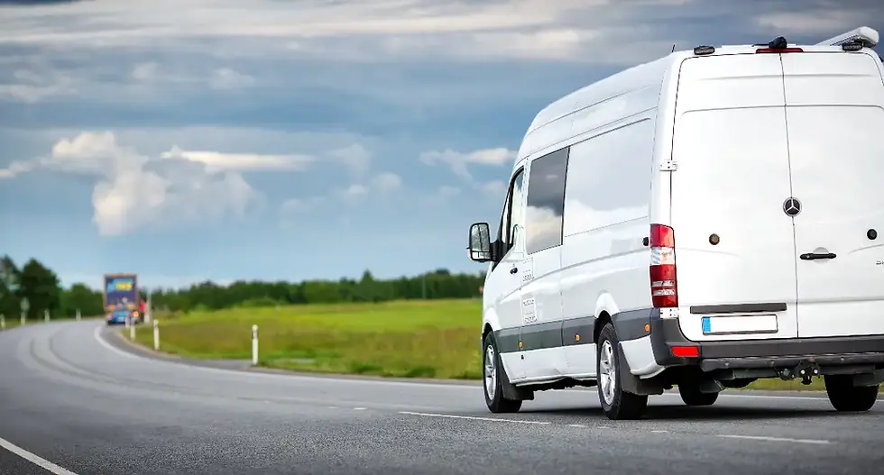White van driving on a road, trees and field visible in the background.