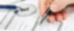 Hand writing on medical forms with pen and stethoscope in background.