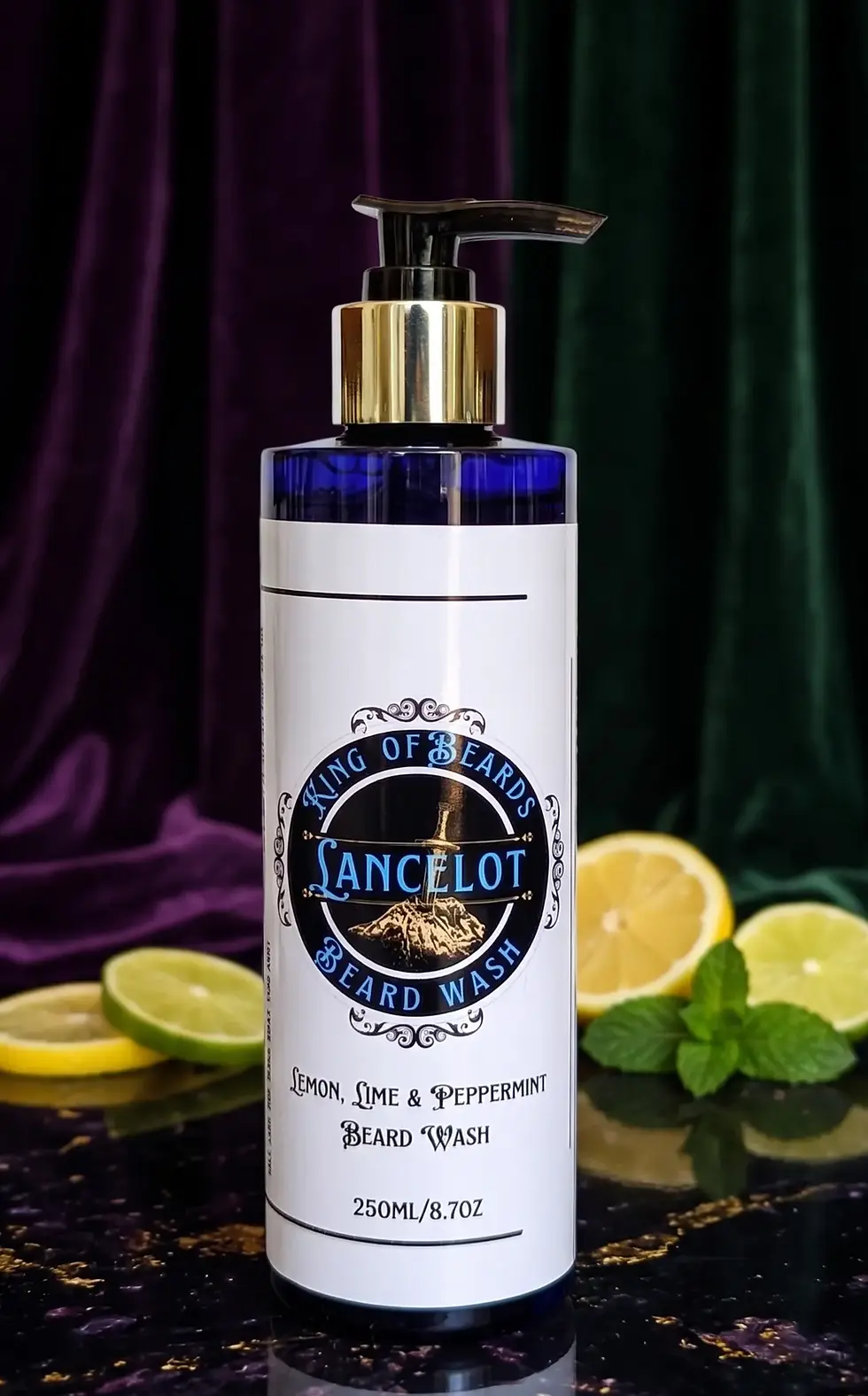 A 250ml blue glass bottle of Lancelot Beard Wash with a gold pump, styled on a dark marble surface with fresh lemon and lime 