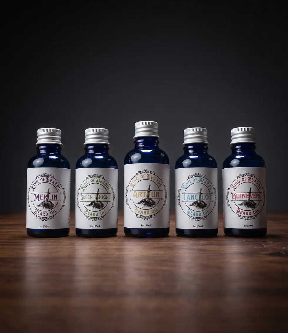 Five blue glass bottles of King of Beards beard oil—Merlin, Green Knight, Arthur, Lancelot, and Guinevere—standing upright