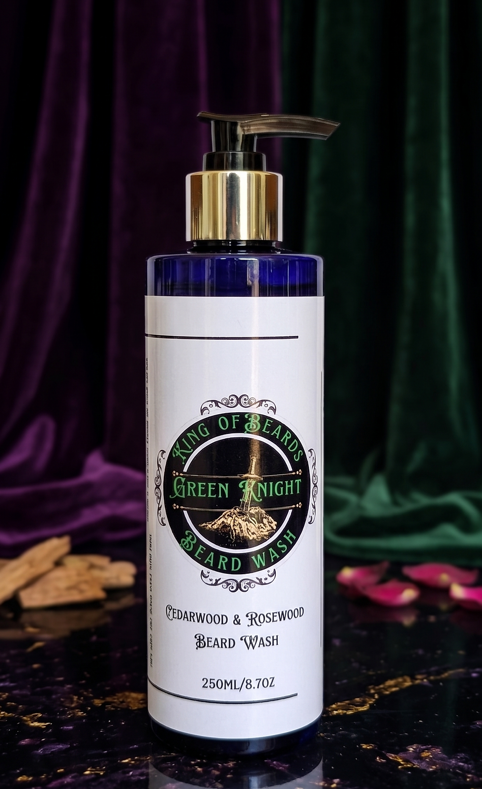 A 250ml bottle of Green Knight Beard Wash with a gold accent pump, styled with aromatic wood shavings and dried botanical pet